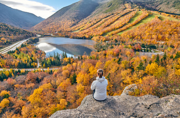 Woman hiking at Artist's Bluff in autumn. View of Echo Lake. Fall colours in Franconia Notch State...