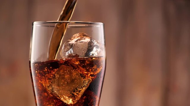 Cola pouring in tall glass thish ice cubes ib slow motion. A lot of bubbles and sparkling.