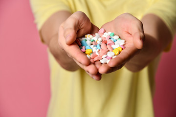 A handsome man in T-shirt on a pink background holding pills in his hand