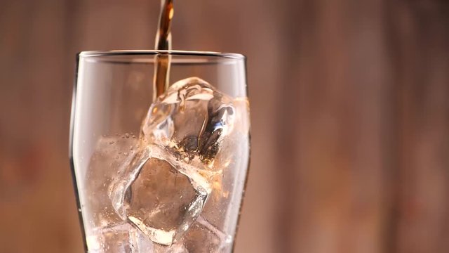 Cola pouring in tall glass thish ice cubes ib slow motion. A lot of bubbles and sparkling.