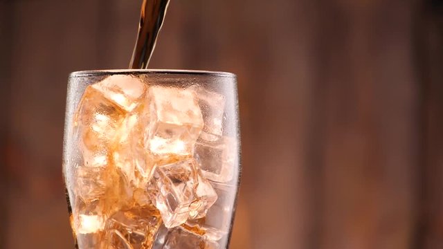 Cola pouring in tall glass thish ice cubes ib slow motion. A lot of bubbles and sparkling.