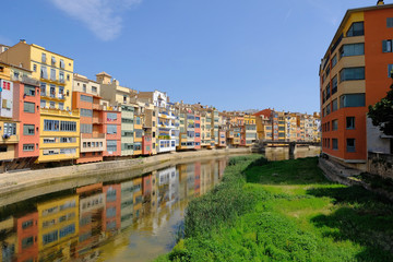 Colorful yellow and orange houses and Eiffel Bridge, Old fish stalls, reflected in water river Onyar, in Girona, Catalonia, Spain. Church of Sant Feliu at background.
