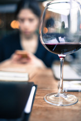 young adult woman busy with her phone behind of a wine glass