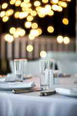 Table setting at a restaurant. Clean glass cup close up. Details of the banquet table. On the background blur are burning garlands with light bulbs