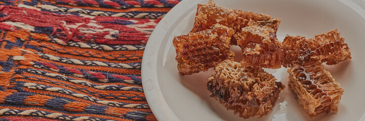 Honeycomb on white plate. Pieces of full honeycomb served on white plate on colorful rug.
