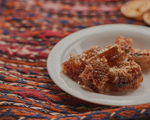 Honeycomb on white plate. Pieces of full honeycomb served on white plate on colorful rug.