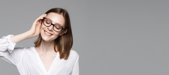 Portrait of young modern business woman. Smiling beautiful slim brunette with equal hair female business leader in casual wear expressing happy emotions. Gray background.