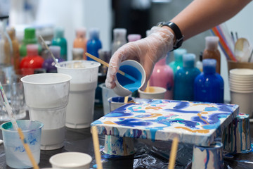 Fototapeta premium Hands of the artist is mixing acrylic paint for her new project, different colors. Artist tools for true art and inspiration. Art studio at background.