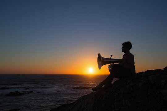 Silhouette of a musician with a tuba on the sea beach during sunset.