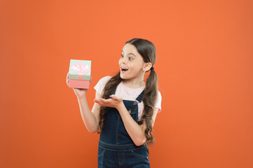 The best present ever. Small child holding birthday present on orange background. Little girl with wrapped present box. Surprised kid receiving present on boxing day