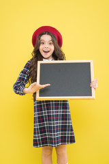 presenting product. small girl in french beret. happy girl with curly hair in beret. advertisement. child with empty blackboard. child on yellow. copy space. school time. presenting school project