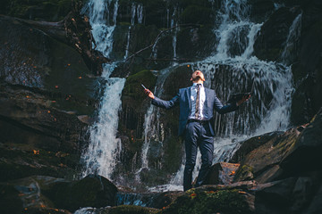 Young handsome man in wet office suit holding Laptop under the water on nature background. Fantasy...