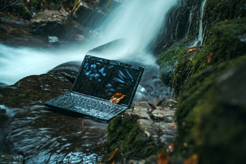 Laptop under the surface of the water on nature background. Testing technology for stability.