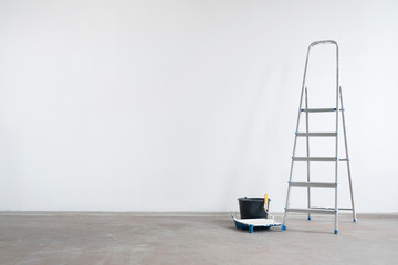Ladder and bucket with paint roller on a white wall background with copy space. Under construction...