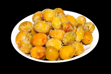 ripe yellow plum with splashes on plate on black isolated background