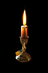 burning candle on an old candlestick on a black isolated background
