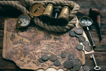 Treasure map and adventurer accessories on a wooden table background. Treasure hunt concept...