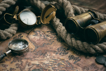 Treasure map and adventurer accessories on a wooden table background. Treasure hunt concept background.