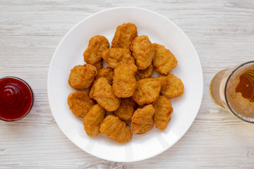 Chicken nuggets on a white plate, ketchup and glass of cold beer on a white wooden background. Overhead, from above, flat lay.