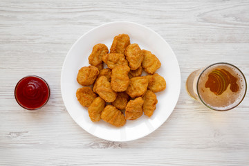 Chicken nuggets on a white plate, ketchup and glass of cold beer on a white wooden surface. Overhead, from above, flat lay.