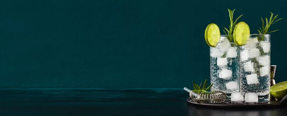 Foto op Plexiglas banner van klassieke gin-toniccocktail met rozemarijntakjes in hoge glazen op een tafel met baraccessoires © irinagrigorii