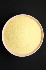 Dry semolina durum flour in a pink bowl over black surface, top view. From above, overhead, flat lay. Close-up.