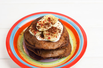 gluten-free chocolate pancakes, proper diet vegetarian food for breakfast with cocoa, Greek yogurt and banana on a colorful rainbow colored plate of LGBT flag colors. LGBT breakfast concept on white 