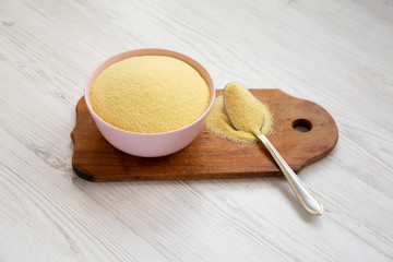 Dry semolina durum flour in a pink bowl over white wooden surface, low angle view. Closeup.