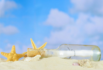 Fototapeta na wymiar Summertime image of a beach scene on sand with a blue sky that has puffy white clouds in the distance. A message in a bottle lays among shells and starfish.