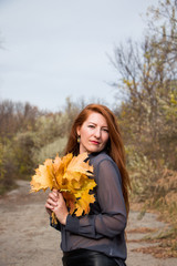 Naklejka premium Portrait of young redhead woman with bouquet of yellow leaves