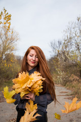 Naklejka premium Portrait of young redhead woman with bouquet of yellow leaves