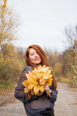 Naklejka premium Portrait of young redhead woman with bouquet of yellow leaves