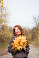 Portrait of young redhead woman with bouquet of yellow leaves