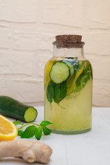 Natural belly slimming detox Sassy Water in a jar with ingredients (lemon, mint, ginger, cucumber) on white wooden table
