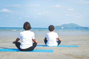 Two elderly women sitting on the sand, doing yoga by the sea