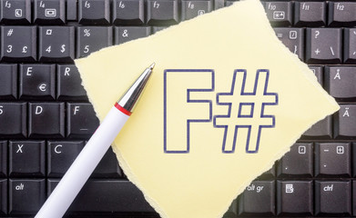 F sharp programming language. Paper width word F# and pencil on laptop keyboard