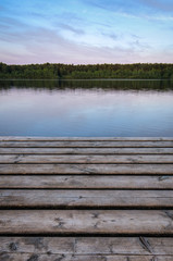 Fototapeta na wymiar Wooden pier at the lake on the background of the forest. Early morning. The vertical frame.