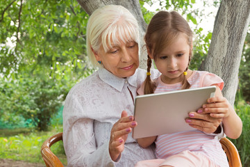Grandmother with her granddaughter studying a book on a tablet, work on the tablet. Granny at the...