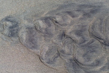 Dark sand on beach with traces of water. Sand on the river. Traces of waves hollowed out in sand on beach