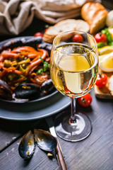 A glass of dry white wine on the background of Italian cuisine. Pasta, mussels and wine.