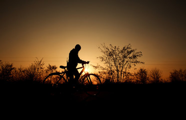 Silhouette of a boy with bicycle on background of bright sunset sun in vintage old style