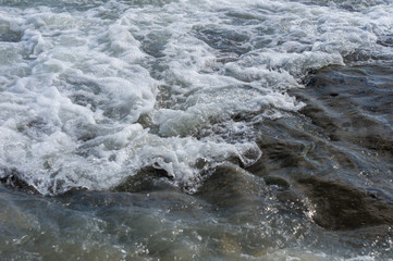 pebble stones on the sea beach, the rolling waves of the sea with foam