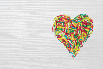 Multicolored heart shaped sticks isolated on white wooden background with copy space.