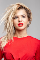 Young blond girl with a red  lipstick short  in a red t-shirt poses staying against a wall in the studio 