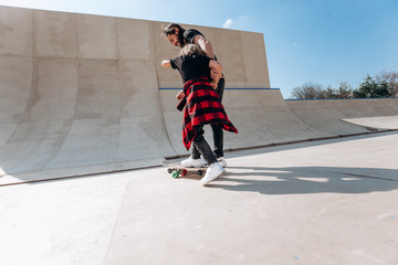 Father and his little son dressed in the casual clothes ride skateboards in a skate park with slides at the sunny day