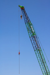 Fototapeta premium Close up shot of green crane arm. Blue sky. Hook and reel
