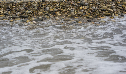 pebble stones on the sea beach, the rolling waves of the sea with foam