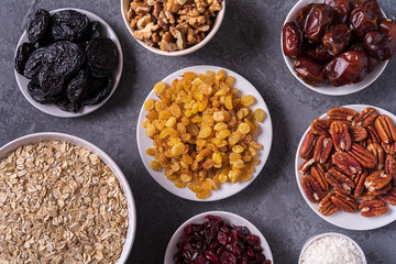 Ingredients for preparing Healthy organic energy balls- dates, dried apricot, oat flakes, raisin, dried cranberries, pecan nuts, coconut shavings on gray background.