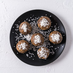 Healthy organic energy balls made with dates, prunes, raisins, peanut, with coconut shavings, in black plate on white background.