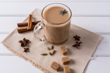Obraz na płótnie Canvas Masala chai tea in a glass mug and kitchen herbs, over white table background.